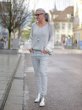 Frau auf dem Bürgersteig trägt OFF#DLY Pant Tina grey, leichte Joggpant mit Kettenkordel, Gummibund und Taschen. Kombiniert mit silbernen Stiefeln und langem Pullover, modisch und bequem.