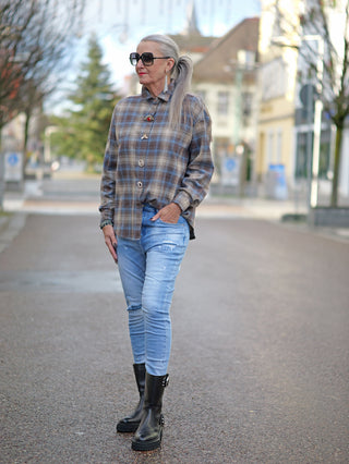 Frau trägt OFF#DLY Bluse Bella beige/blue mit Karomuster und verdeckter Knopfleiste, kombiniert mit blauer Jeans und schwarzen Stiefeln auf der Straße.