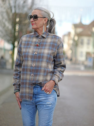 Frau trägt die OFF#DLY Bluse Bella beige/blue, eine karierte Oversize-Bluse mit verdeckter Knopfleiste und Broschen, kombiniert mit blauer Jeans und Sonnenbrille.