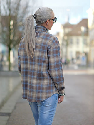 OFF#DLY Bluse Bella beige/blue: Frau trägt oversized karierte Bluse mit verdeckter Knopfleiste und Broschen, kombiniert mit blauer Jeans. Ideal für lässige Outdoor-Mode.
