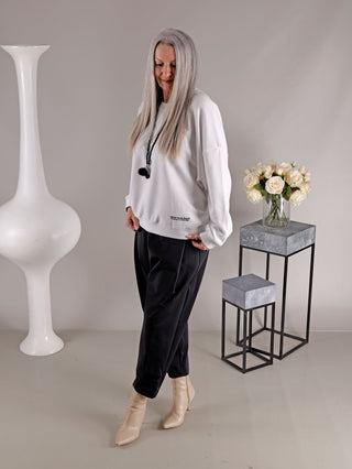 Frau trägt Liv Bergen Ella Dream optic white Sweatshirt vor Blumenvase, locker geschnitten mit Rundhalsausschnitt und neon Print, passend in Größe S, ideal für lässigen Stil.