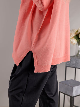 Person in einem rosa Pullover, bekannt als OFF#DLY Pulli Olivia apricot, trägt schwarze Hose. Der Pullover hat eine gerade Passform und ist aus Viskose, Polyester und Polyamid gefertigt.
