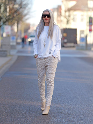 OFF#DLY Hose Mixa beige: Frau mit langen grauen Haaren trägt schmal geschnittene Joggpant mit Gummizug und Taschen, kombiniert mit weißem Hemd und Sonnenbrille, präsentiert im Freien.
