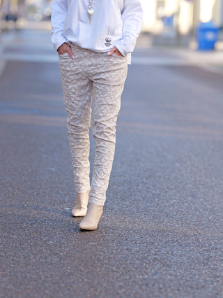 OFF#DLY Hose Mixa beige: Person trägt schmale Joggpant mit Gummizug und weißen Stiefeln, sichtbare Vordertaschen. Stoffdetails und Passform betonen modernes Street-Fashion-Design.