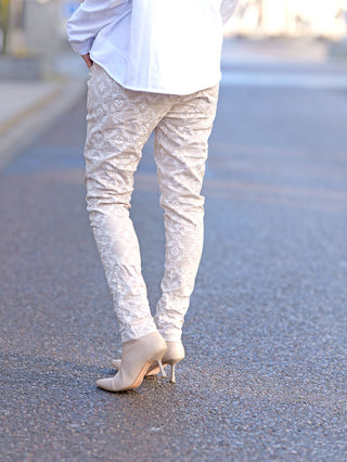 OFF#DLY Hose Mixa beige: Person trägt schmale Joggpant mit Gummizug und Absatzschuhen, Vorder- und Gesäßtaschen sichtbar, Allover-Print-Design, passend für Größen bis 42.
