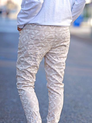 OFF#DLY Hose Mixa beige, schmale Joggpant mit Allover-Print, Gummizug und Taschen vorne. Person in weißem Shirt und beige Hose, zeigt die Passform und Design der Hose.