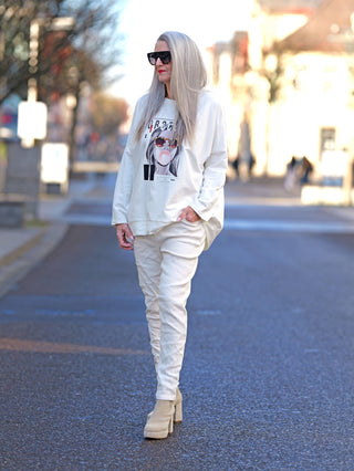 Frau trägt den OFF#DLY Sweat obscure white mit glitzerndem Frontprint, während sie auf der Straße geht. Gerade Passform, ideal bis Größe 44. Aus 100% Baumwolle.