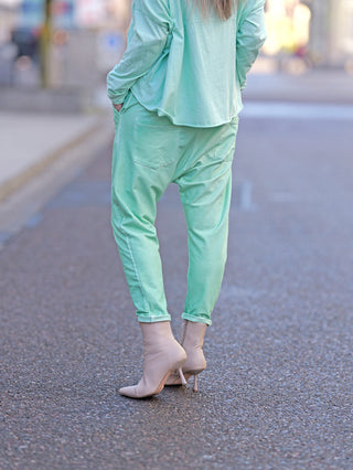 Eine Person trägt die OFF#DLY Jogger Pant Tina türkis. Die Hose hat eine lässige Baggy-Passform mit Gummibund, Kordelzug und seitlichen Taschen. Sie wird mit Absätzen kombiniert.