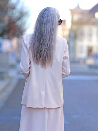 Frau in einem weißen Anzug trägt den OFF#DLY Blazer Bibi apricot mit einem Knopf und angedeuteten Seitentaschen, perfekt für ein elegantes, modisches Straßenoutfit. Passform: Gerade.