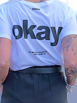 Liv Bergen Tee OKAY optic white, getragen von tätowierter Person, zeigt Rundhalsausschnitt und Rückenprint. Gerade Passform, Material aus 100% Baumwolle, detailreiches Design.