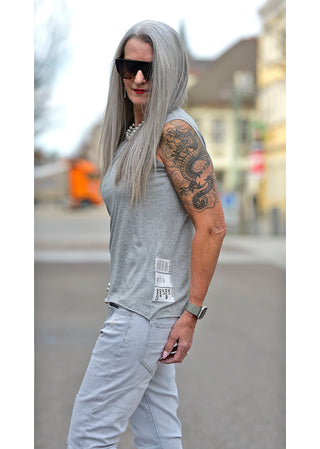 Liv Bergen Top EAST Melange, getragen von einer Frau mit Tattoo auf dem Arm, Rundhalsausschnitt, gerade Passform, kleine Patches sichtbar, kombiniert mit Sonnenbrille in einem lässigen, modischen Outdoor-Setting.