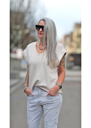 Frau mit langen grauen Haaren trägt Liv Bergen V Shirt in dirty white, kombiniert mit Sonnenbrille, Kette und Armbanduhr, Hände in Jeanstaschen, zeigt lässigen Freizeitstil.