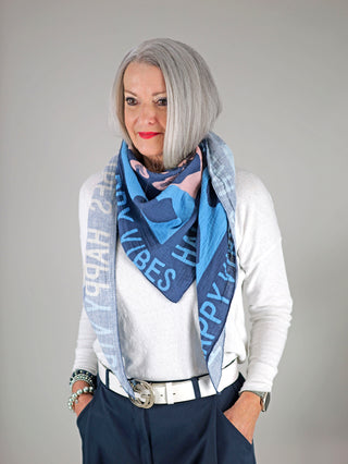 Eine Frau trägt das OFF#DLY Tuch Happy Vibes navy/multi, ein großes Musselin-Dreieckstuch mit Print, locker um den Hals gelegt. Im Bild sind auch Details eines Armbands erkennbar.