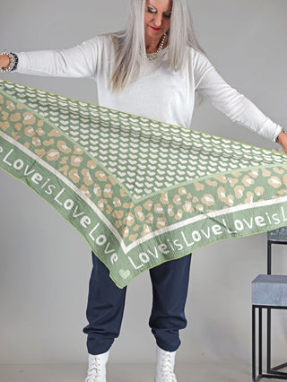 Eine Frau hält das OFF#DLY Tuch LOVE khaki, ein großes Musselin-Dreieckstuch mit Print, aus 100% Baumwolle, Größe ca. 195x95 cm, ideal für stilvolle Akzente.