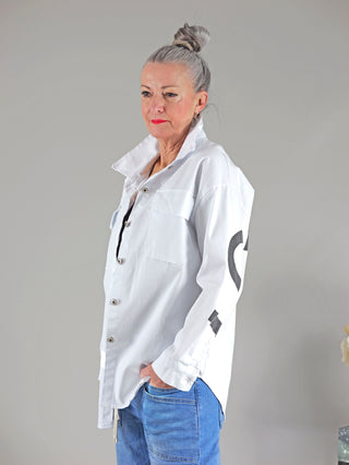 Frau trägt OFF#DLY Bluse London white mit Knopfleiste und Brusttaschen, zeigt eine Hand in der Jeanstasche. Das Hemd hat einen LONDON-Druck auf der Rückseite.