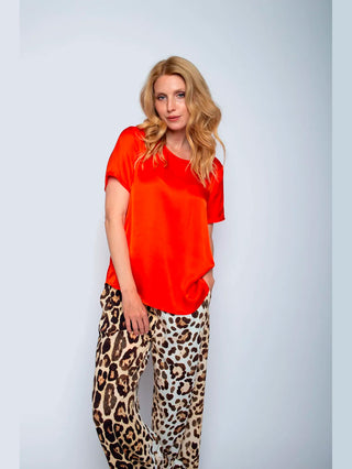 Emily Bluse Fire 156100: Eine Frau trägt ein rotes Rundhals-Shirt mit Halbarm und offenen Kantenblenden, kombiniert mit einem Leopardenmuster-Rock, aus 100% Viskose-Satin.