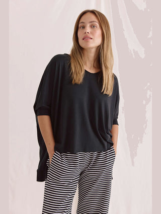 Frau trägt das Cotton Candy Tee Helay black: ein oversized schwarzes Shirt mit V-Ausschnitt und gerippten Ärmeln, kombiniert mit gestreiften Hosen.