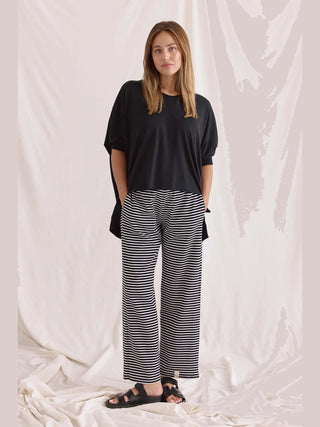 Frau trägt das Cotton Candy Tee Helay black, ein oversized schwarzes T-Shirt mit V-Ausschnitt und gerippten Ärmeln, kombiniert mit gestreiften Hosen.
