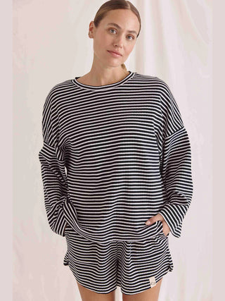 Frau trägt das Cotton Candy Tee Fjolla im schwarz/weiß gestreiften Design mit langen Ärmeln und Oversized-Passform. Das Shirt bietet durch die Materialzusammensetzung hohen Tragekomfort.