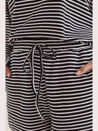 Eine Person trägt die Cotton Candy Short Hefron Stripes mit schwarz-weißen Streifen, lässigem Schnitt, seitlichen Eingrifftaschen und Tunnelzug, aus bequemem, geripptem Material.