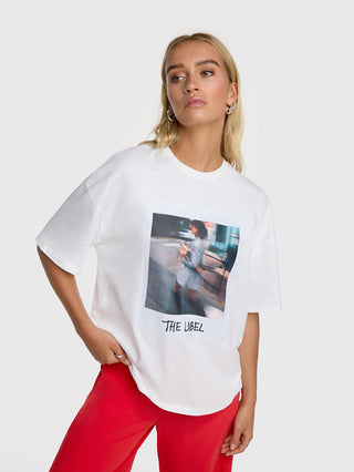 Die ALIX Polaroid Tee in Weiß zeigt einen Polaroid-Print vorne und VOLUME 1 hinten. Das T-Shirt hat eine gerade Passform und wird von einer Frau getragen.