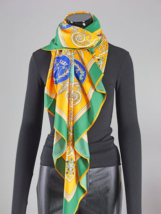 Mannequin trägt OFF#DLY Schal Horse green/orange, ein gemustertes Viskosetuch, drapiert um den Hals. Größe: 130x130 cm. Pflegehinweis: Handwäsche. Hersteller: Monopol Modevertriebs GmbH & Co KG.