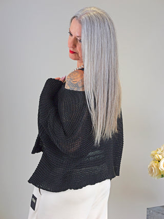 Eine Frau mit langem grauem Haar trägt die OFF#DLY Jacke Manuela black, eine stilvolle Grobstrickjacke mit Einknopfverschluss, sichtbar über der Schulter tätowiert.