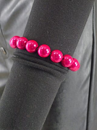 OFF#DLY Kugelarmband 12mm pink Magic, ein pinkfarbenes, glänzendes Acrylarmband mit runden Perlen, präsentiert auf einem schwarzen Stoffärmel. Ein modisches Accessoire, das Eleganz und Stil vereint.