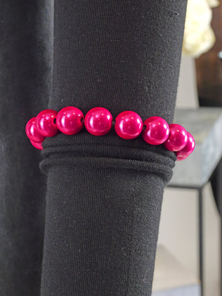 OFF#DLY Kugelarmband 12mm pink Magic liegt auf schwarzem Stoff, bestehend aus glänzenden, rosa Acrylperlen, die elegant aneinandergereiht sind. Ein stilvolles Schmuckstück für modische Akzente.
