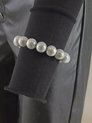 OFF#DLY Kugelarmband 12mm grey Magic: Ein weißes Perlenarmband auf schwarzem Stoff, bestehend aus glanzenden Acrylperlen, das als modisches Accessoire getragen wird.