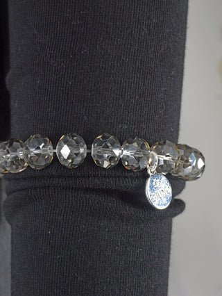 Glasperlenarmband OFF#DLY grau, präsentiert auf schwarzem Hintergrund. Der Nahaufnahme zeigt funkelnde Kristallperlen und silberne Akzente, die das modische Schmuckstück elegant zur Geltung bringen.