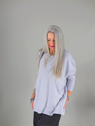 OFF#DLY Pulli Olivia hellgrau: Frau trägt locker sitzenden, hellgrauen Pullover mit geradem Schnitt, kombiniert mit schwarzen Hosen, silberner Kette und Armbändern.