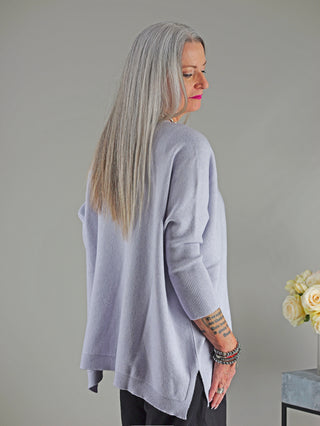 Frau mit langem grauem Haar trägt den OFF#DLY Pulli Olivia hellgrau, ein gerade geschnittener, normaler Pullover, perfekt für Größen 34 bis 46. Detail: Blumenstrauß im Hintergrund.