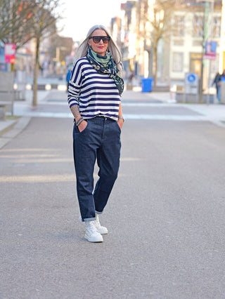 Nuomeno Denim Carrot blue: Frau in gestreiftem Shirt trägt stylische dunkelblaue Jeans mit seitlichen Einschubtaschen und elastischem Bund, stehend auf der Straße.