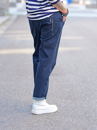 Eine Person trägt die Nuomeno Denim Carrot blue Jeans mit seitlichen Einschubtaschen und großen Rückentaschen. Die Jeans hat einen elastischen Bund hinten und passt in Regular Carrot Fit.