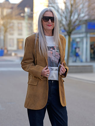 Frau trägt den OFF#DLY Blazer Lin braun, einen stylischen Longblazer aus Kunstleder in Wildlederoptik mit zwei Knöpfen und seitlichen Taschen, kombiniert mit Sonnenbrille.