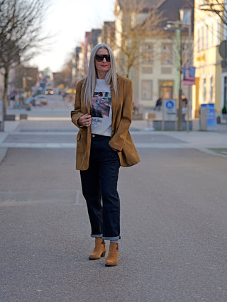 Frau trägt den OFF#DLY Blazer Lin braun, einen stylischen, langen Kunstlederblazer in Wildlederoptik mit zwei Knöpfen und seitlichen Taschen, kombiniert mit blauer Jeans und braunen Stiefeln.