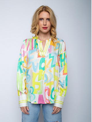 Emily Bluse 8564-152710 multi/letters: Frau trägt bunte Shirtbluse mit Stehkragen, V-Ausschnittblende, Streifenmanschetten und lockerer Passform. Fließender Viskose Satin mit Letterprint. 