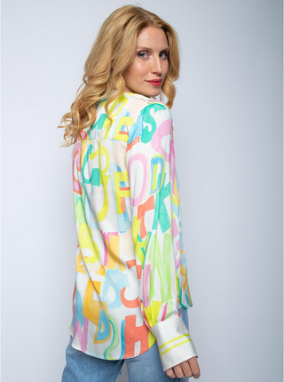 Emily Bluse 8564-152710 multi/letters: Frau mit blonden Haaren trägt eine bunte Shirtbluse mit Stehkragen, V-Ausschnitt, langen Ärmeln und Buchstabenprint auf fließendem Viskose Satin.