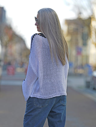 Frau trägt den OFF#DLY Pulli Ulrike weiß, sportiver Netzpulli mit schwarzer Seitennaht, auf der Straße. Sichtbar sind der Rundhals und die verkürzten Ärmel. Perfekt für legere Street Fashion.