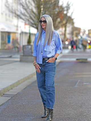 Nuomeno Concept Bluse Corta bianco, getragen von einer Frau auf dem Gehweg, zeigt eine stylische Boxy-Passform mit weiten 3/4 Ärmeln und großer Brusttasche.