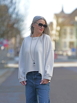 Frau trägt den Nuomeno Sweat 21014164 tofu, ein cooler Boxy-Sweater mit verkürzten Ärmeln. Sichtbar ist ein 3D-Logo-Print am Rücken, kombiniert mit einer Sonnenbrille.