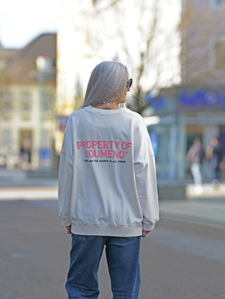 Nuomeno Sweat 21014164 tofu: Frau mit grauen Haaren trägt boxy geschnittenen Sweater mit verkürzten Ärmeln und 3D-Logo auf dem Rücken, kombiniert mit blauen Jeans, auf einer Straße stehend.