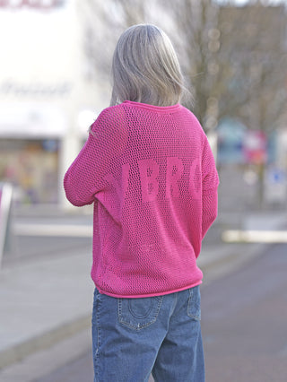 Liv Bergen Crochet Sweater Pink, getragen von einer Frau, zeigt einen lockeren Schnitt aus Netzstoff mit LVBRGN-Schriftzug auf der Rückseite. Lange Ärmel und gerade Passform, aus 100% Baumwolle.