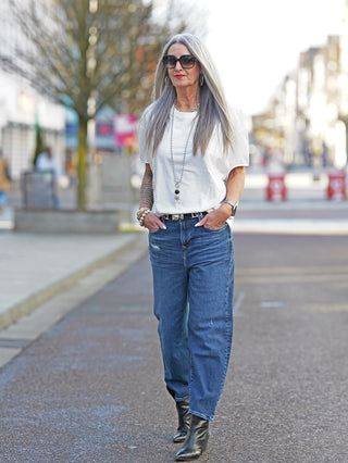 Frau trägt das Nuomeno Concept Tee Trapezio tofu, ein oversized ärmelloses Shirt mit Rundhalsausschnitt, während sie auf dem Gehweg geht. Jeans und Schuhe ergänzen den Look.