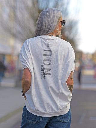 Frau trägt das Nuomeno Concept Tee Trapezio tofu mit Oversized-Schnitt und Rundhalsausschnitt. Rückenprint sichtbar. Kombiniert mit Jeans, ideal für lässige Streetwear.