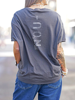Nuomeno Concept Tee Trapezio grafite, ärmelloses Oversized-Shirt mit Rundhalsausschnitt und Rückenprint, getragen von tätowierter Person in blauen Jeans, betont Street-Fashion-Stil.