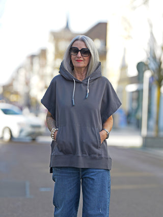 Nuomeno Hoody 14164 Grafite: Frau trägt einen oversized grauen Hoody mit Kapuze und Rückenprint auf der Straße, kombiniert mit blauen Jeans und Sonnenbrille. Ideal für street fashion.
