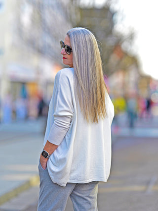 Frau mit langen Haaren trägt den OFF#DLY Basic Pulli Zitta weiß mit Rundhals und 3/4 Ärmeln. Der Pulli hat eine boxy Passform und ist hinten länger geschnitten.