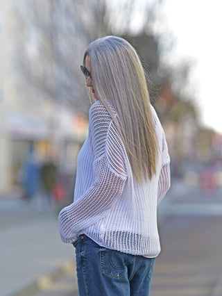 Eine Frau trägt den OFF#DLY Netzpulli Leila offwhite mit Rundhalsausschnitt und langen Ärmeln. Der lässige, gerade geschnittene Pulli ist aus Baumwolle, ideal für Street Fashion.